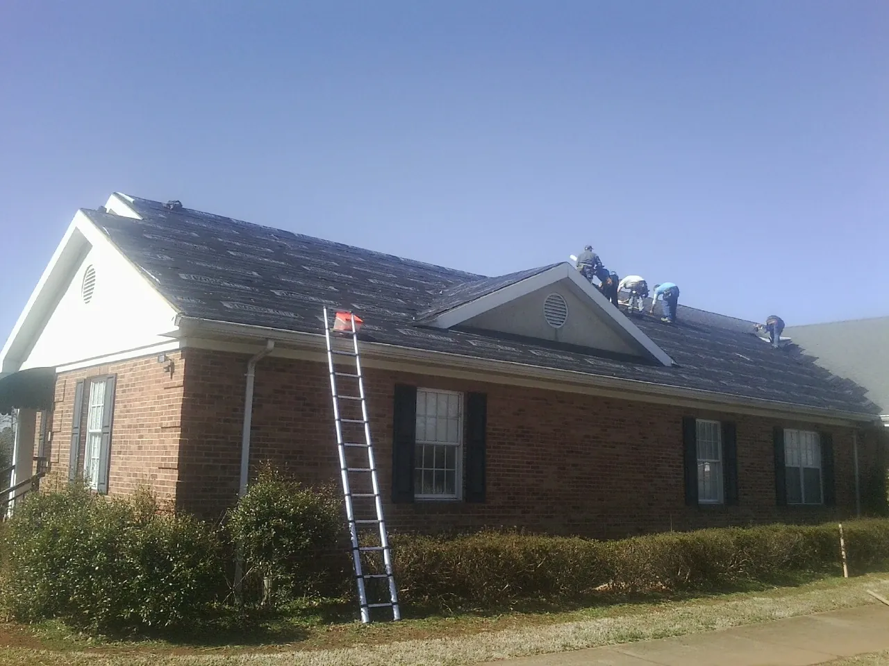 Crew tearing shingles off a brick ranch roof with a ladder set — Emergency Roof Repair work by our crew in Manning