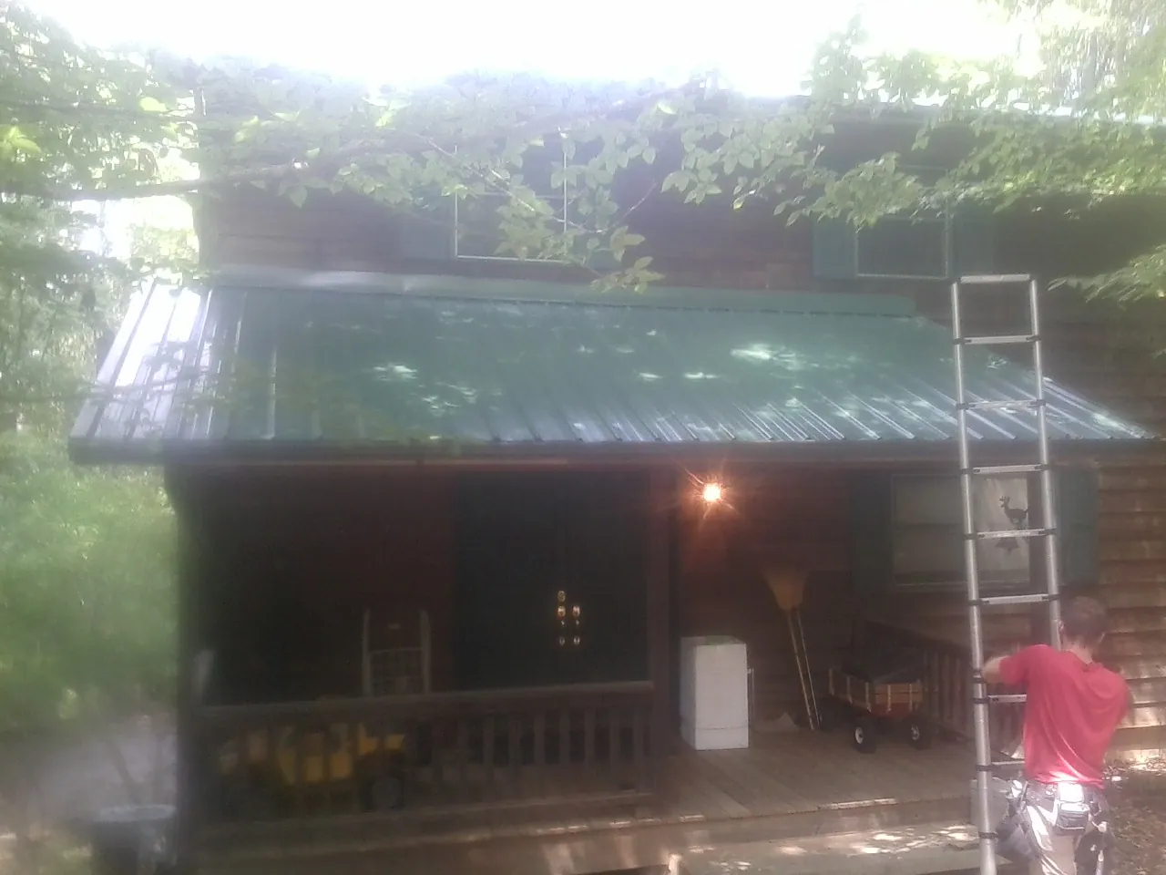 Worker on a ladder at the green porch roof of a wooded cabin in Manning